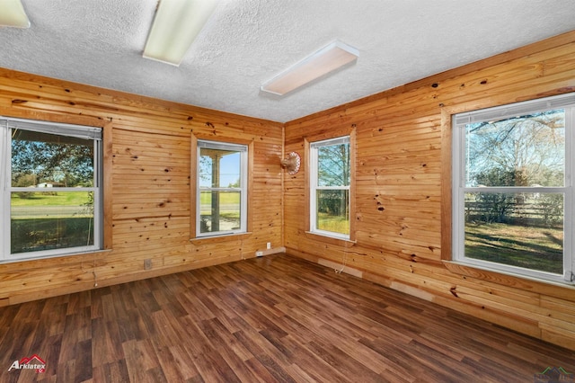 empty room featuring wooden walls, a wealth of natural light, and dark wood-type flooring