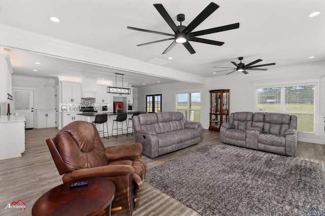 living room with a wealth of natural light, light wood-style floors, ornamental molding, and recessed lighting