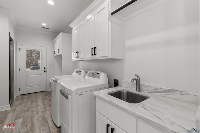 laundry area with light wood finished floors, washing machine and clothes dryer, cabinet space, ornamental molding, and a sink