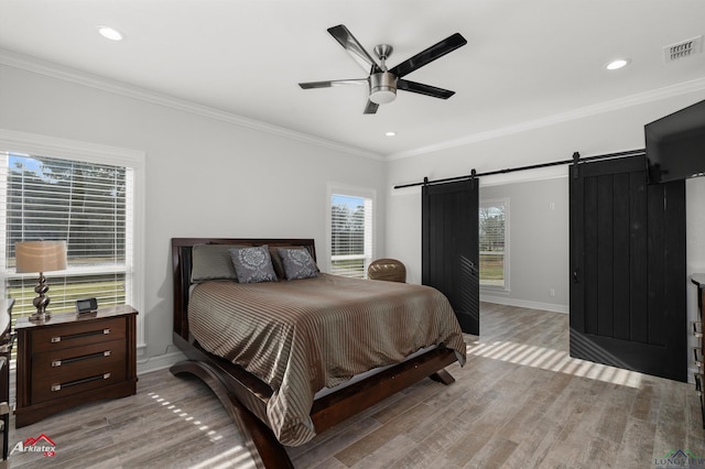 bedroom featuring light wood-type flooring, a barn door, baseboards, and ornamental molding