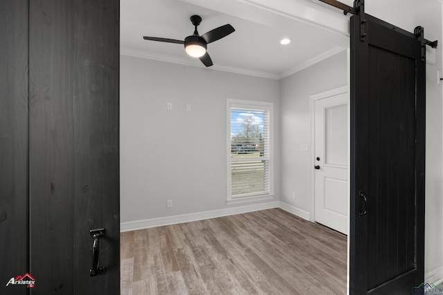 unfurnished room featuring baseboards, light wood-style flooring, ceiling fan, ornamental molding, and a barn door