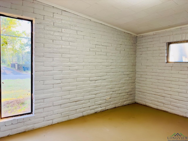 basement featuring a wealth of natural light, crown molding, and brick wall