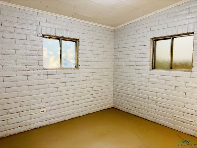 unfurnished room with concrete flooring, crown molding, and brick wall