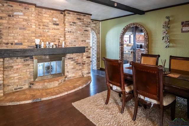 dining area with a brick fireplace, ornamental molding, beam ceiling, and wood finished floors