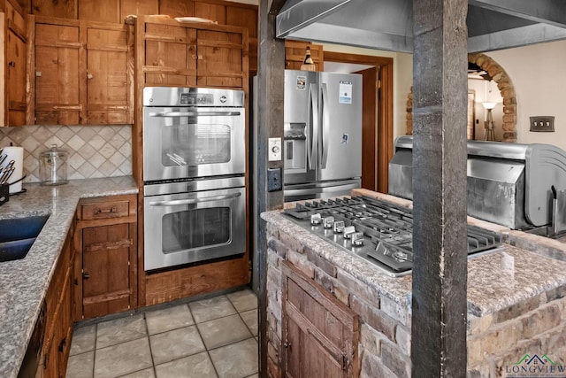 kitchen featuring light stone counters, stainless steel appliances, brown cabinets, and decorative backsplash