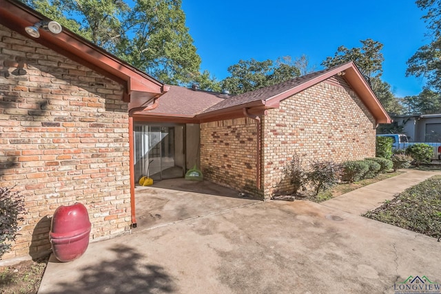 view of side of property featuring brick siding, a shingled roof, and a patio