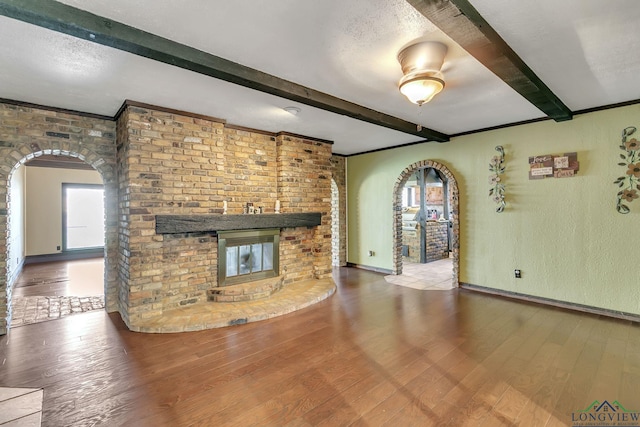 unfurnished living room featuring arched walkways, a textured ceiling, wood finished floors, and beam ceiling