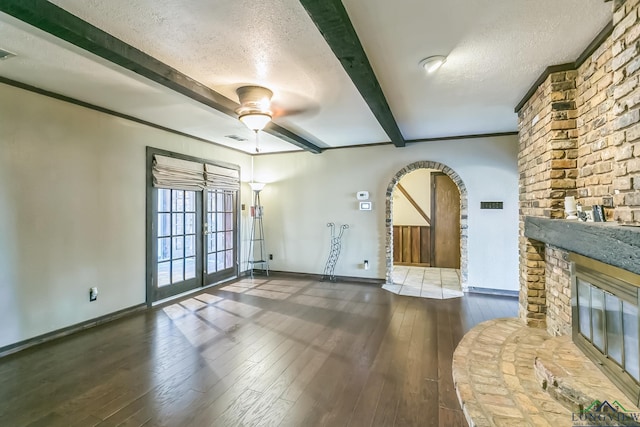 unfurnished living room featuring a textured ceiling, hardwood / wood-style flooring, a ceiling fan, beam ceiling, and arched walkways