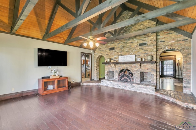 unfurnished living room featuring baseboards, arched walkways, beam ceiling, hardwood / wood-style flooring, and a brick fireplace