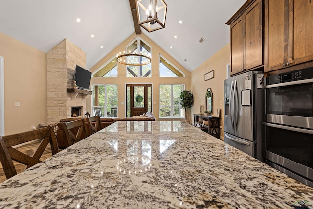 kitchen with a breakfast bar area, light stone countertops, a fireplace, a notable chandelier, and stainless steel appliances