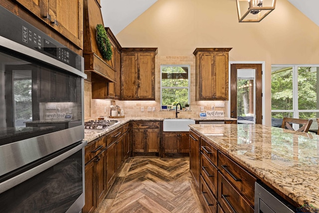 kitchen with dark parquet flooring, high vaulted ceiling, sink, light stone counters, and stainless steel appliances