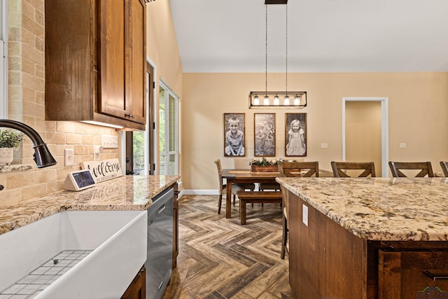 kitchen featuring pendant lighting, dishwasher, sink, light stone counters, and a breakfast bar area