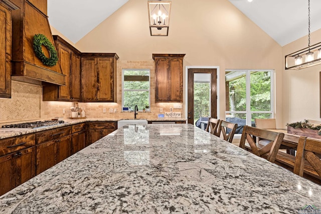 kitchen with decorative backsplash, light stone countertops, sink, and high vaulted ceiling