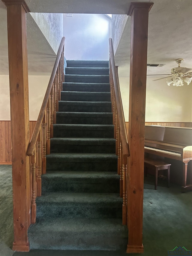 staircase with a textured ceiling, ceiling fan, and carpet flooring
