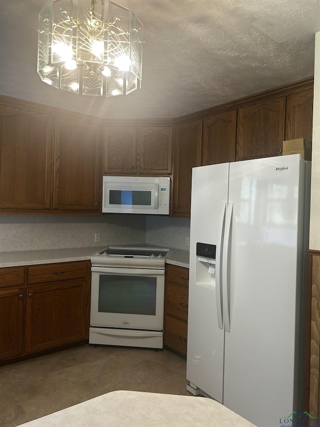 kitchen featuring light countertops, a textured ceiling, a notable chandelier, and white appliances