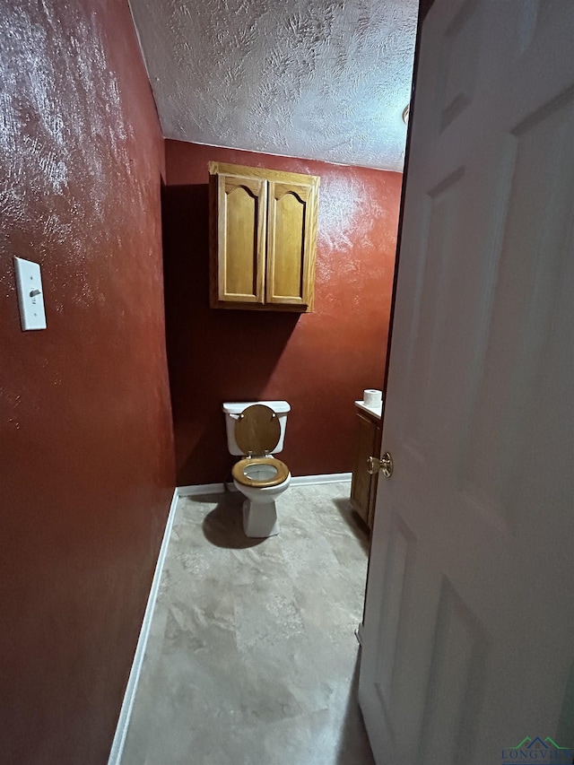bathroom with toilet, a textured ceiling, vanity, and baseboards