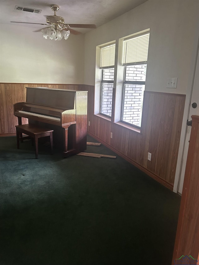 living area with a ceiling fan, visible vents, wainscoting, and wood walls