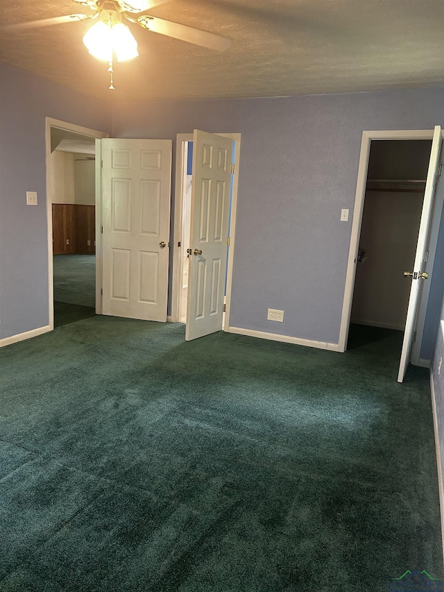 unfurnished bedroom featuring a walk in closet, baseboards, a ceiling fan, and carpet floors