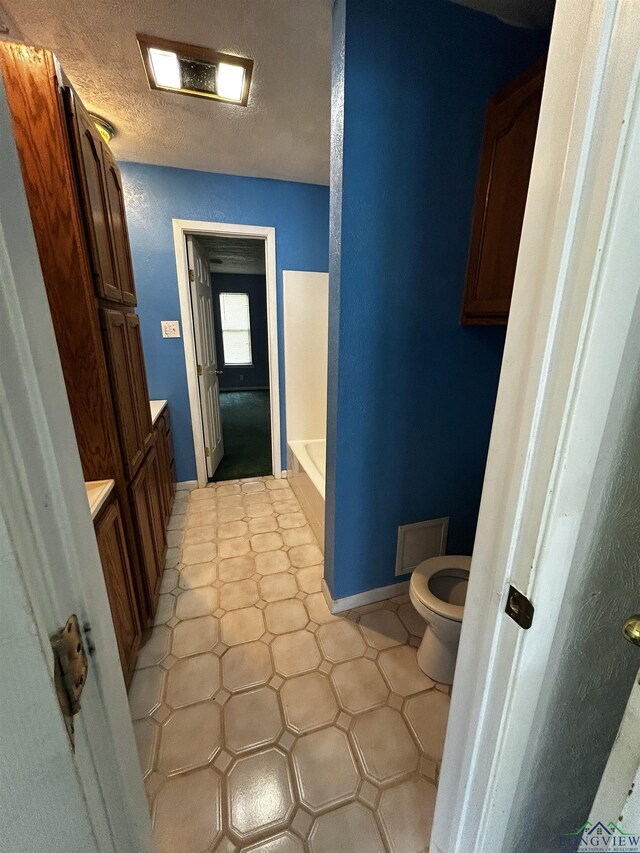 bathroom with a washtub, toilet, vanity, baseboards, and visible vents