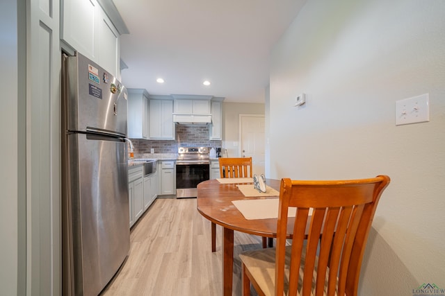 kitchen featuring under cabinet range hood, light countertops, appliances with stainless steel finishes, decorative backsplash, and light wood finished floors