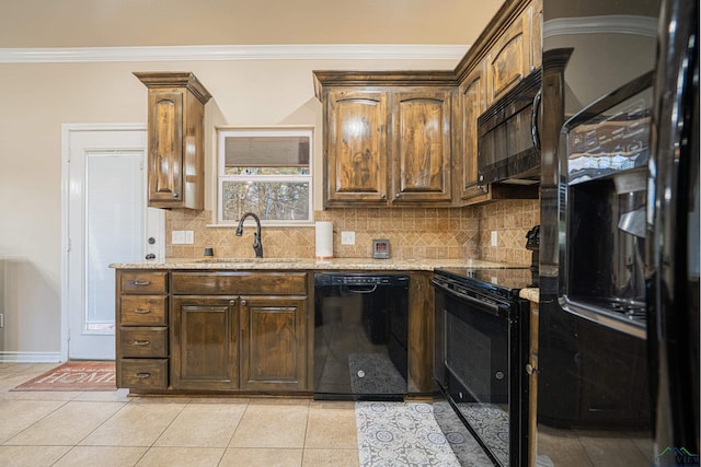 kitchen featuring light stone counters, a sink, decorative backsplash, black appliances, and crown molding