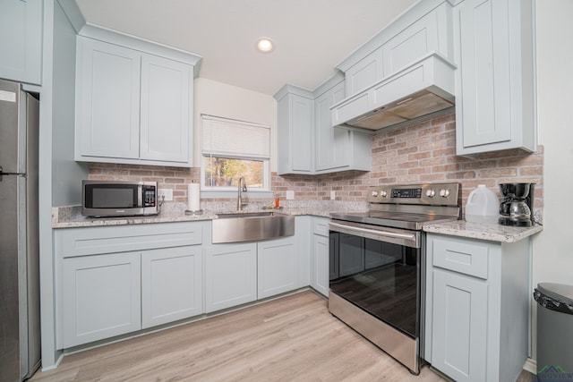 kitchen with stainless steel appliances, a sink, light wood-type flooring, tasteful backsplash, and custom range hood