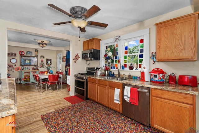 kitchen featuring sink, ceiling fan, light stone countertops, light wood-type flooring, and stainless steel appliances