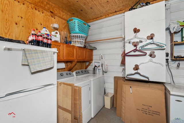 clothes washing area featuring washing machine and dryer, wood walls, and cabinets