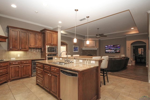 kitchen featuring a kitchen island with sink, sink, a raised ceiling, and appliances with stainless steel finishes