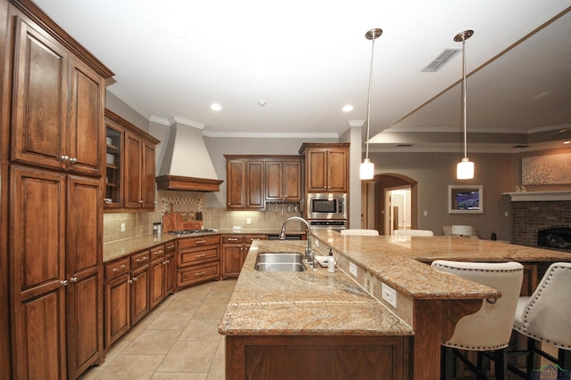 kitchen featuring appliances with stainless steel finishes, sink, a kitchen breakfast bar, a large island with sink, and custom range hood