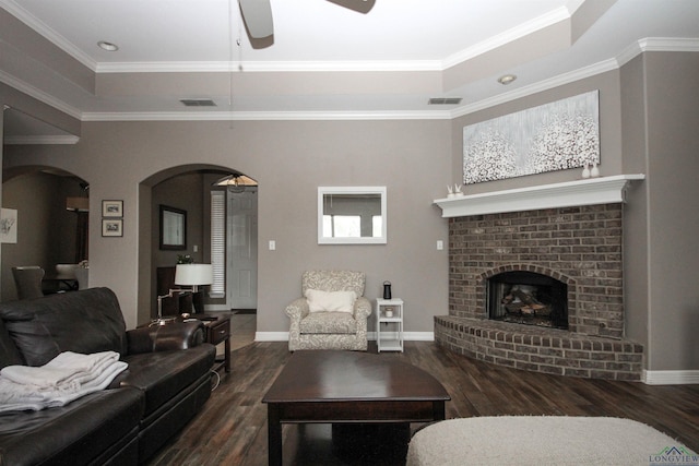 living room with a tray ceiling, a fireplace, ornamental molding, and dark wood-type flooring