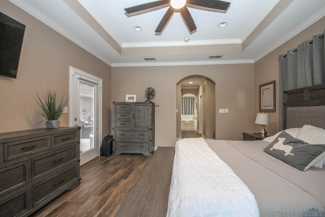 bedroom featuring ornamental molding, dark wood-type flooring, ensuite bath, and a tray ceiling