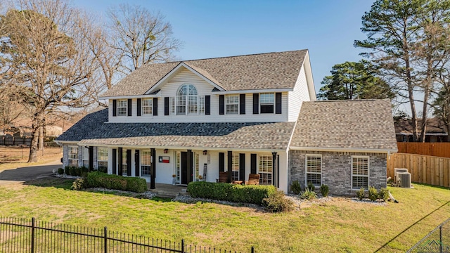 view of front of house featuring a porch, central AC, a shingled roof, fence, and a front yard