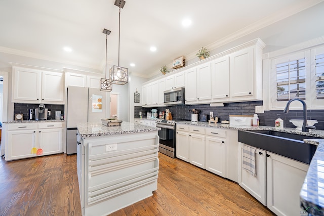 kitchen featuring crown molding, stainless steel appliances, white cabinets, a sink, and wood finished floors