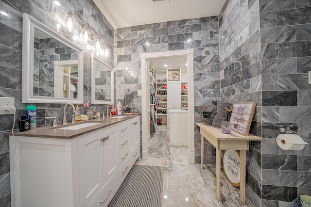 full bathroom featuring marble finish floor, a spacious closet, tile walls, and a sink