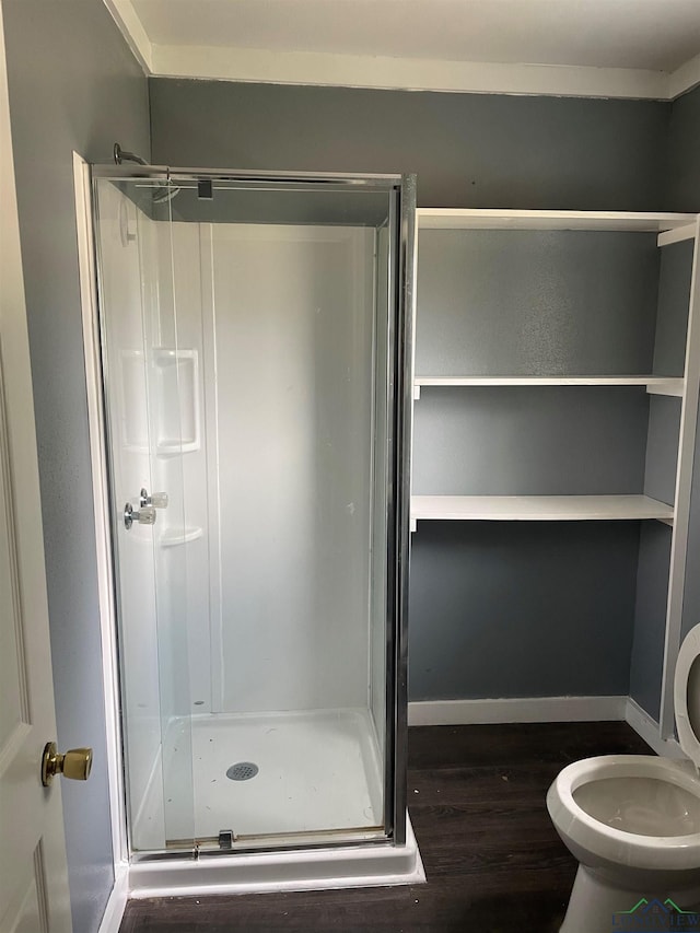 bathroom with toilet, a stall shower, baseboards, and wood finished floors