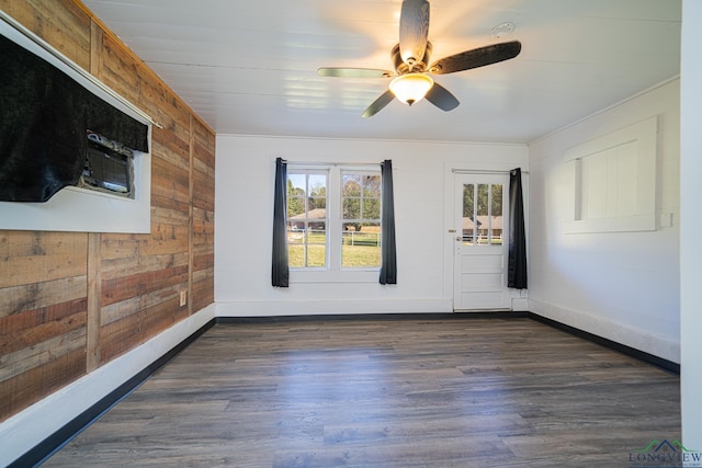 empty room with baseboards, a ceiling fan, wooden walls, and dark wood-style floors