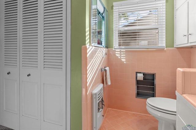 bathroom featuring tile patterned flooring, heating unit, toilet, vanity, and tile walls