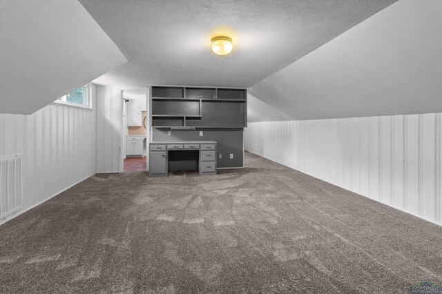 bonus room with dark colored carpet, a textured ceiling, and lofted ceiling