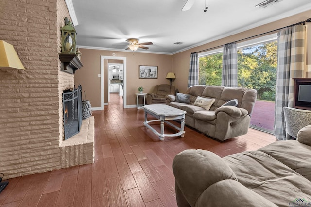 living room featuring hardwood / wood-style flooring, ceiling fan, ornamental molding, and a brick fireplace