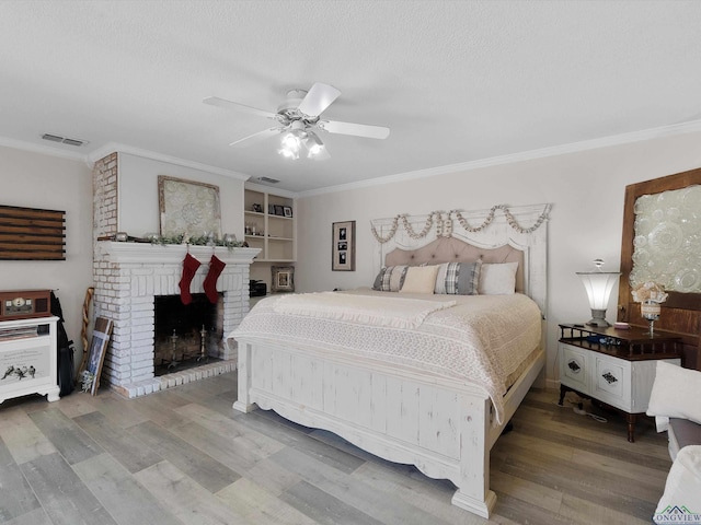 bedroom with ceiling fan, a brick fireplace, wood-type flooring, a textured ceiling, and ornamental molding