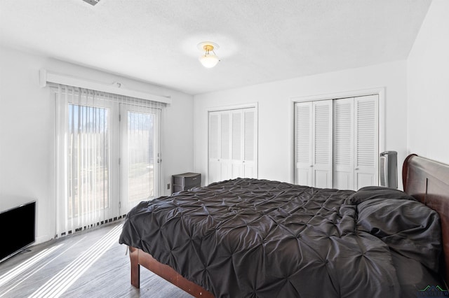 bedroom featuring access to outside, a textured ceiling, two closets, and wood finished floors