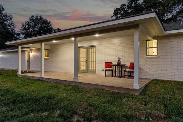 back house at dusk featuring a yard, french doors, and a patio