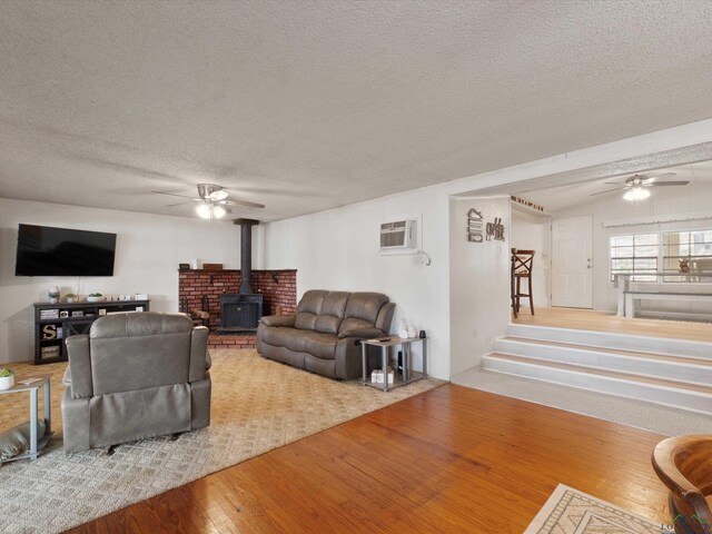 3065 E Lake, Gladewater, TX 75647 - living area featuring a ceiling fan, a wood stove, a textured ceiling, an AC wall unit, and wood finished floors