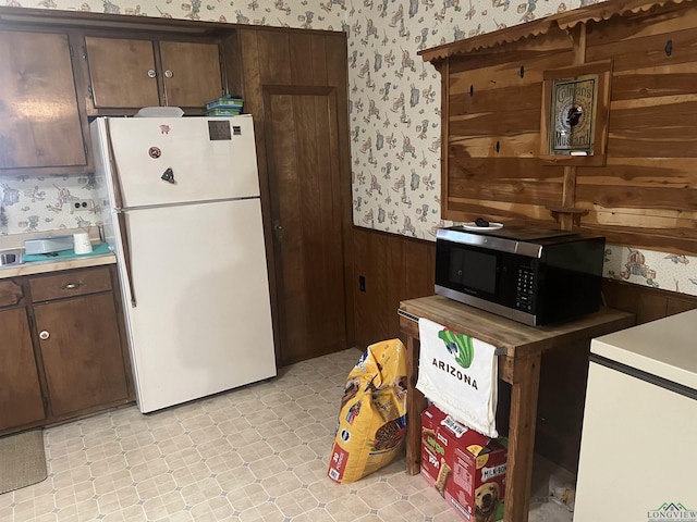 kitchen featuring dark brown cabinetry, wooden walls, and white fridge