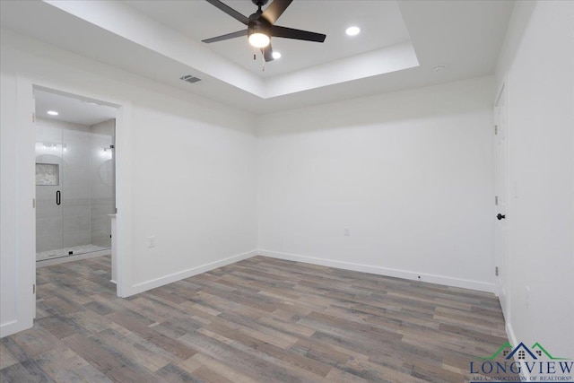 empty room with a tray ceiling, hardwood / wood-style floors, and ceiling fan