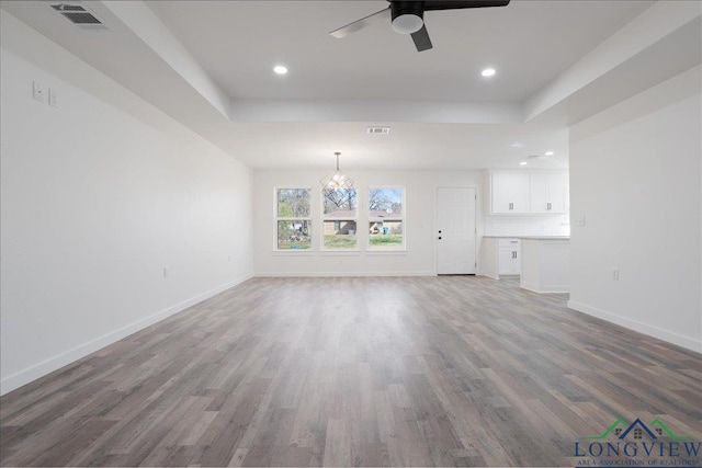 unfurnished living room featuring ceiling fan with notable chandelier, hardwood / wood-style flooring, and a tray ceiling