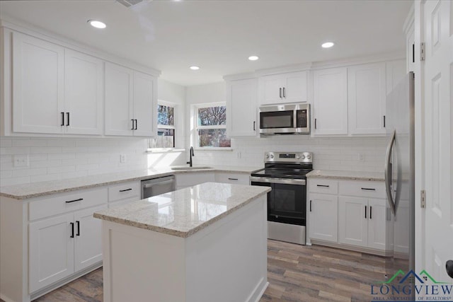 kitchen featuring stainless steel appliances, a kitchen island, light stone countertops, sink, and white cabinets