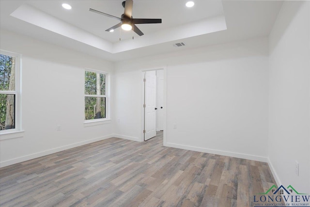 empty room with light hardwood / wood-style floors, a tray ceiling, and ceiling fan