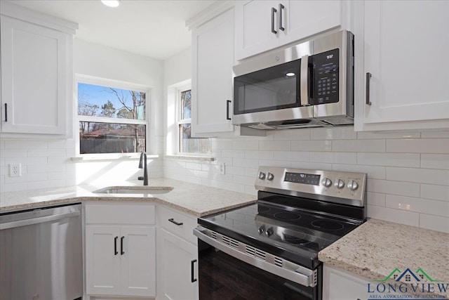 kitchen with appliances with stainless steel finishes, sink, light stone counters, and white cabinets